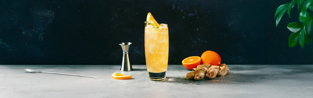 Drinkmate Getränkesprudler: Hintergrundbild mit einem Glas, Orangen und Ingwer für Ingwer-Highball-Spritz-Rezept